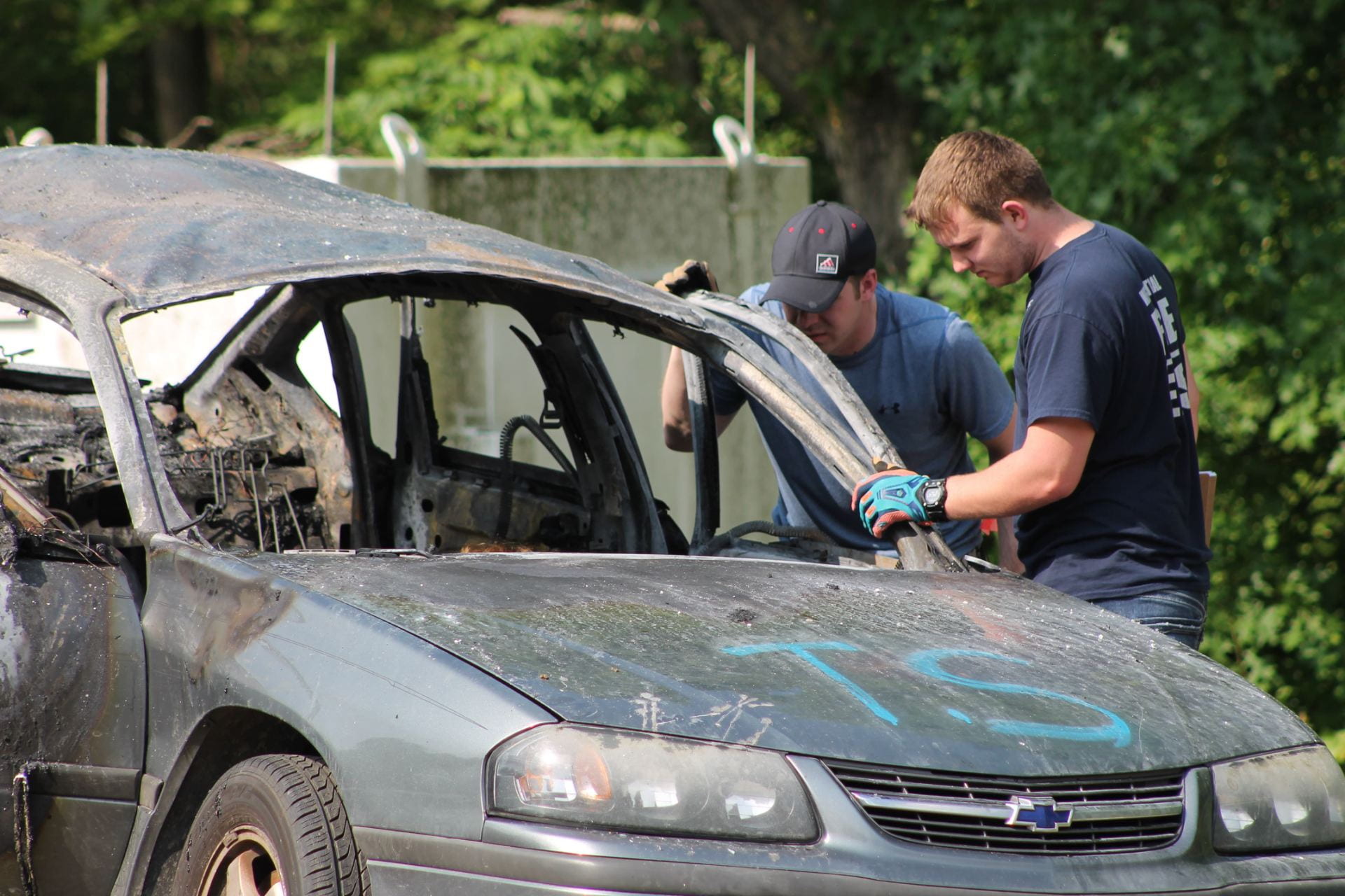 Two students stand beside the burned out remains of a car that had a bomb explode inside of it.