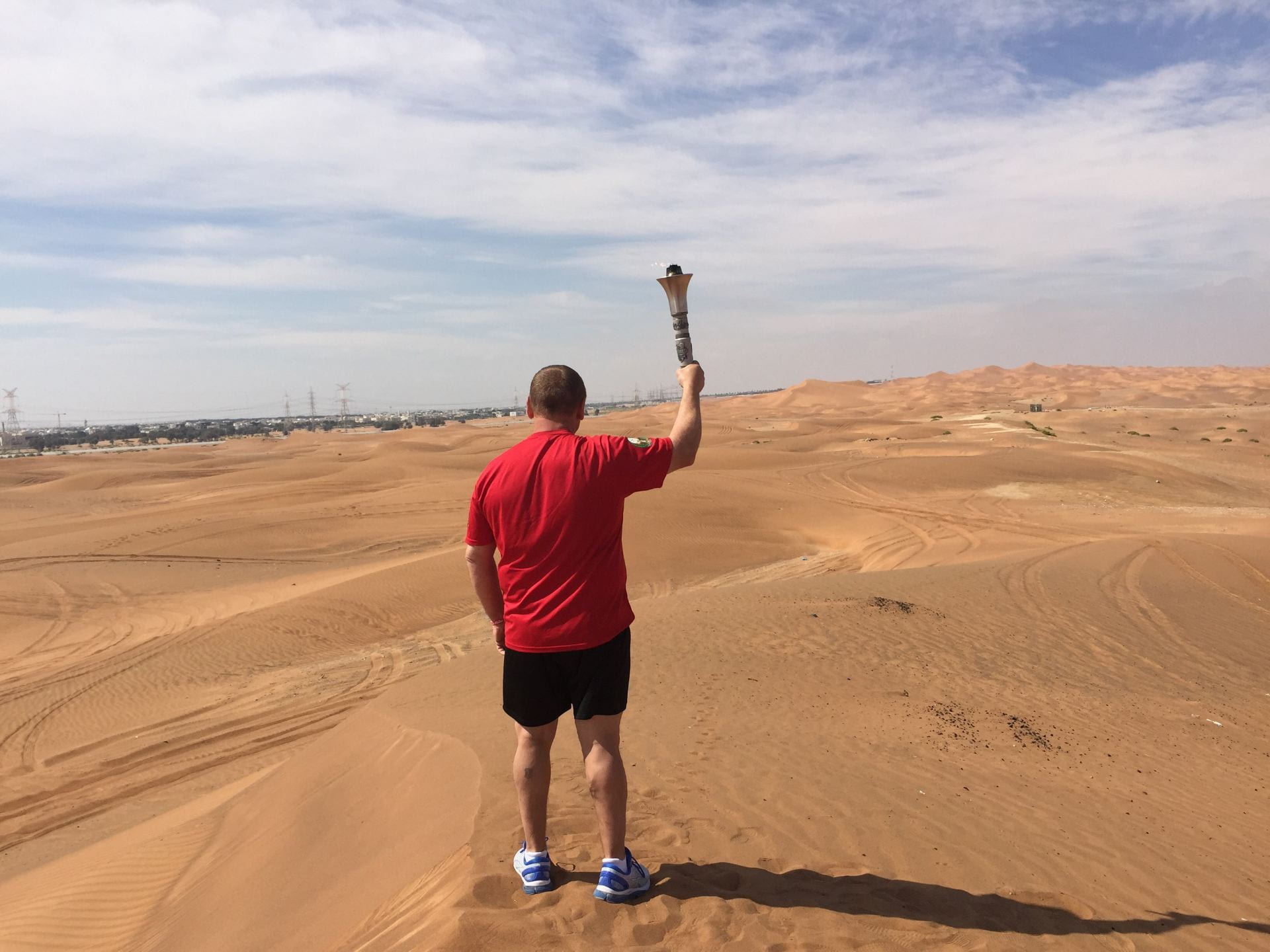Scott Teal stands in the middle of a desert, wearing a red shirt. With his back to the camera, he holds us the Olympic Torch he will carry during the Law Enforcement Torch Run.
