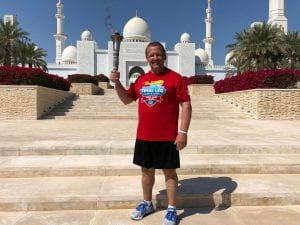 Scott Teal stands outside a white mosque in the United Arab Emirates holding the torch for the Special Olympics 2020 World Games.