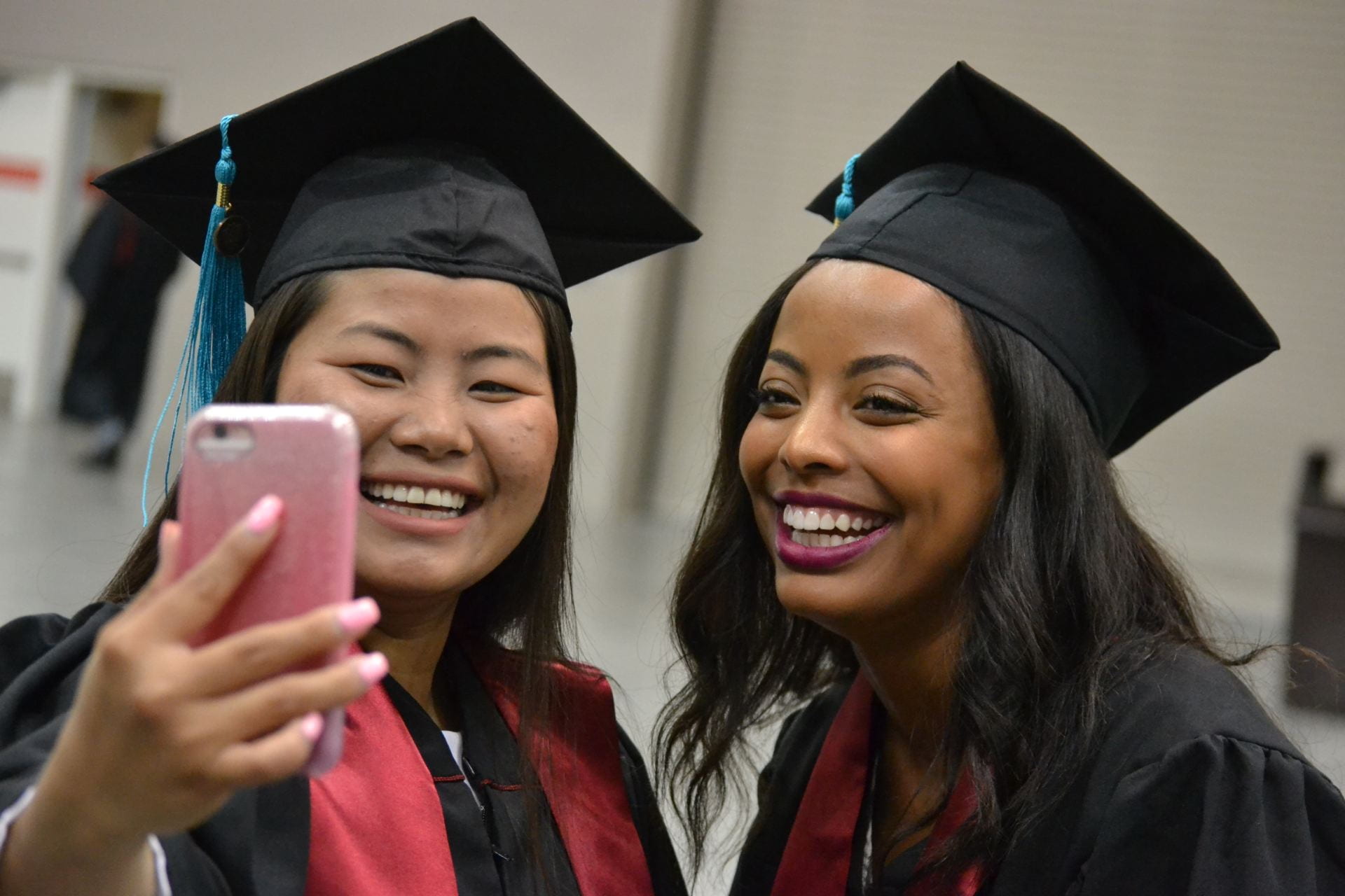 Two women in cap and gowns smile and take a picture at commencement.