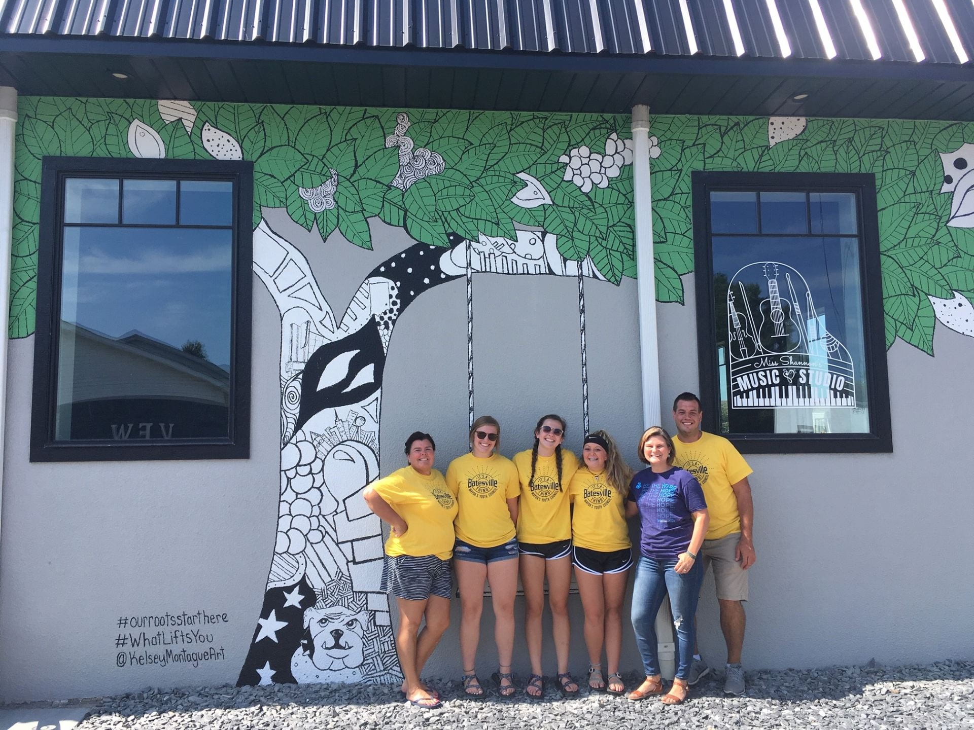 group of teens stand in front of newly painted mural of tree swing.