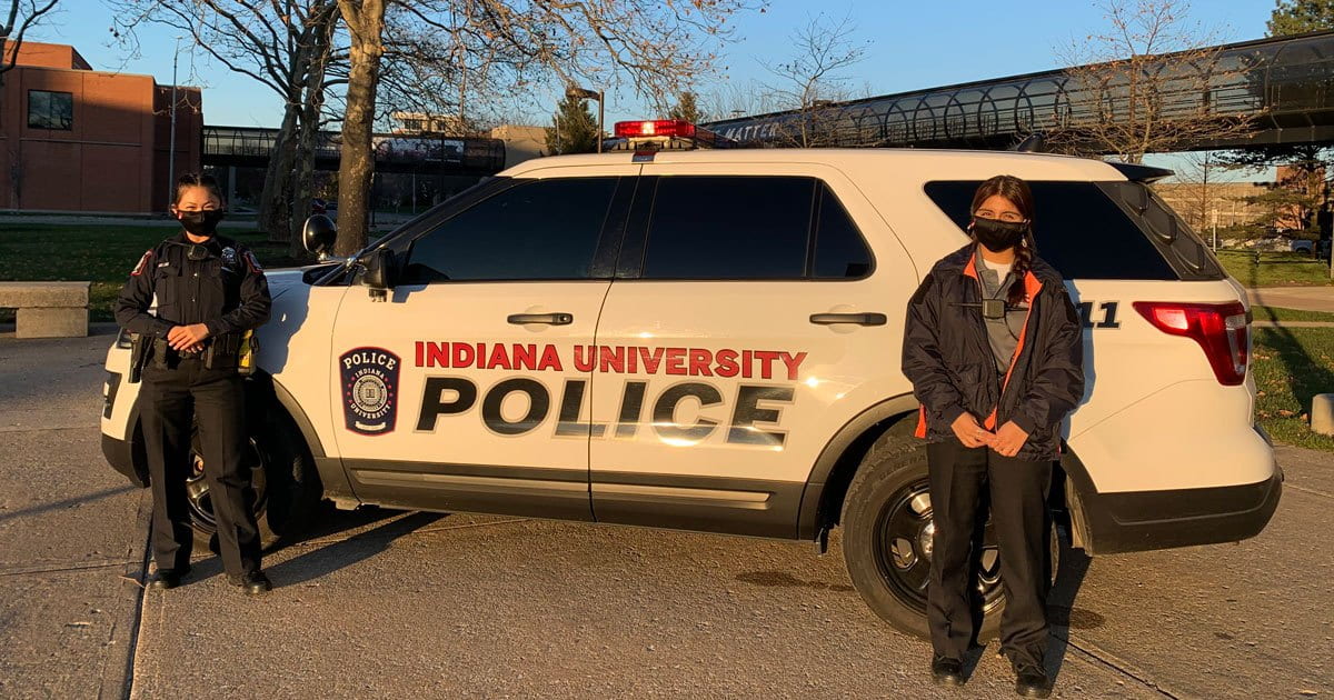Two students stand outside an IUPD vehicle