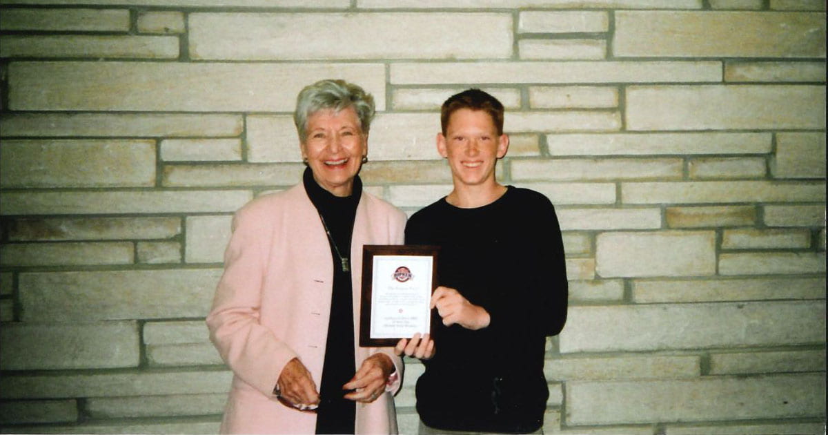 A 12-year-old Aaron McBride holding an award and tanding with his granmother with a limestone wall in the background
