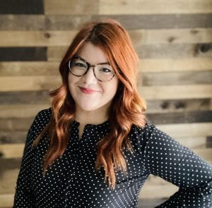 Woman with red hair and glasses wearing a black polka dot shirt
