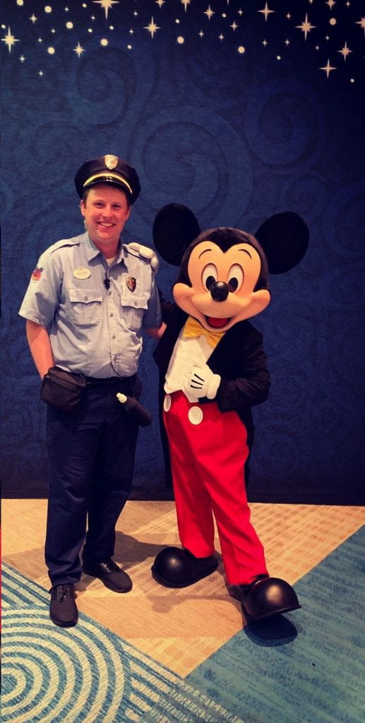 man in security uniform stands with Mickey Mouse
