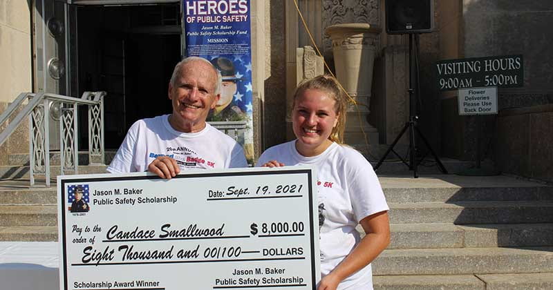 A woman and man stand in white tshirts holding large scholarship check