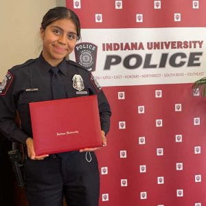 woman standing in police uniform holding diploma in front of IU Police Department backdrop