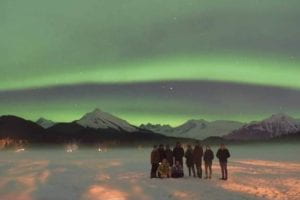group of people standing in the snow with the northern lights behind them in green