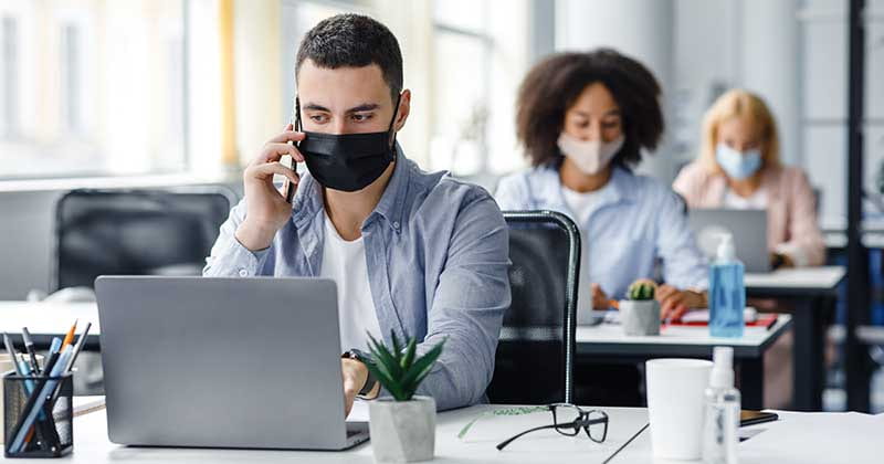 Photo of three people wearing masks in an office typing on laptops