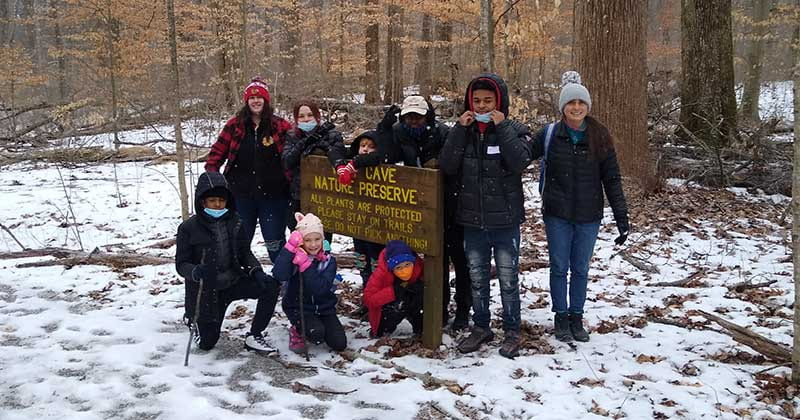 Group photo of children and camp leaders around a state park sign with snow on the ground.