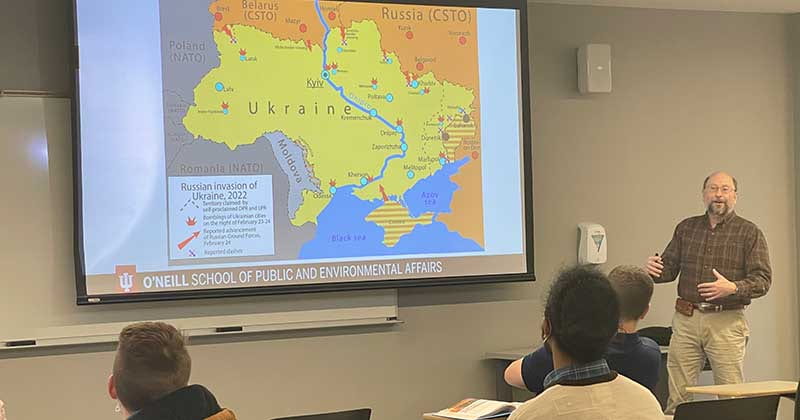 Pierre Atlas lectures students from the front of the classroom with a map of Ukraine behind him 