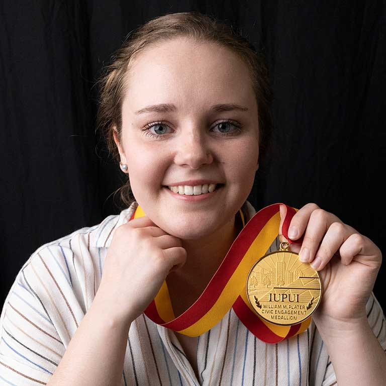 Woman smiles as she holds a medal around her neck.