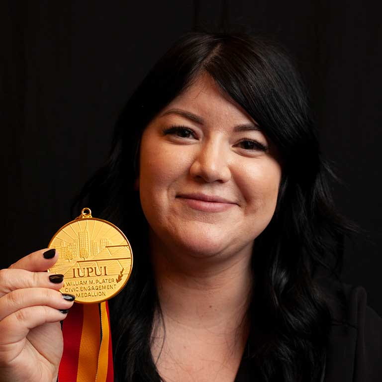 woman smiles while holding golden IUPUI medal in front of her.