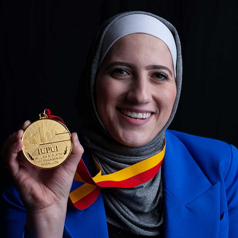 Woman holding a medal she is wearing and smiling