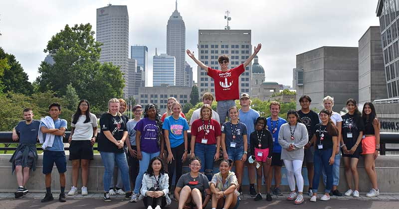 Group of students stand in front of the Indianapolis skyline smiling.