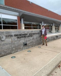 A young man wearing a flannel shirt stands in front of the entry sign for Quantico.