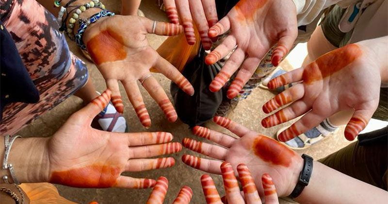 Image of multiple hands in a circle with paint on them in various patterns. 