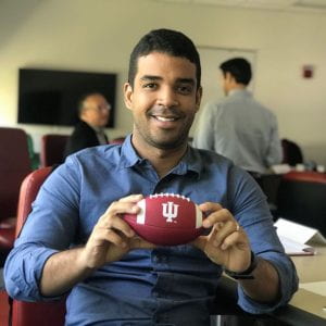 A man sits holding a small red IU Football.